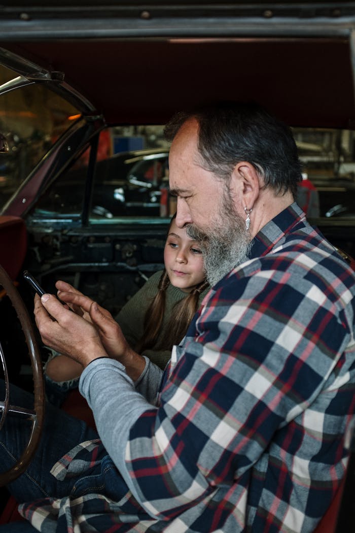 Father and daughter sitting in a car interior viewing a smartphone together, capturing family bonding.