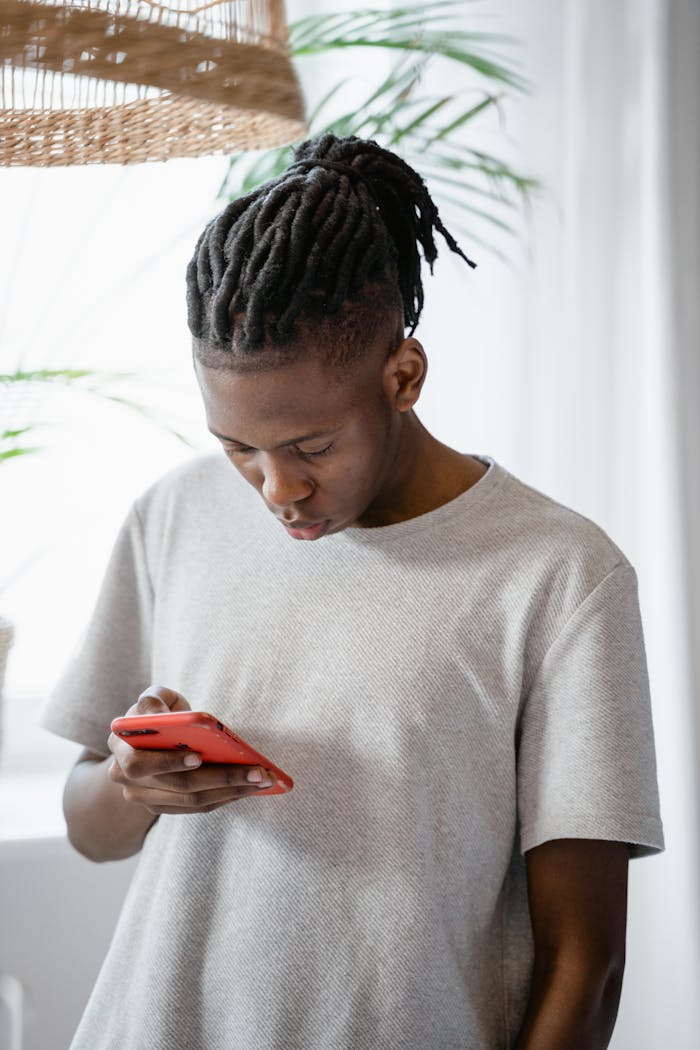 A young man focused on texting with a smartphone, standing indoors.